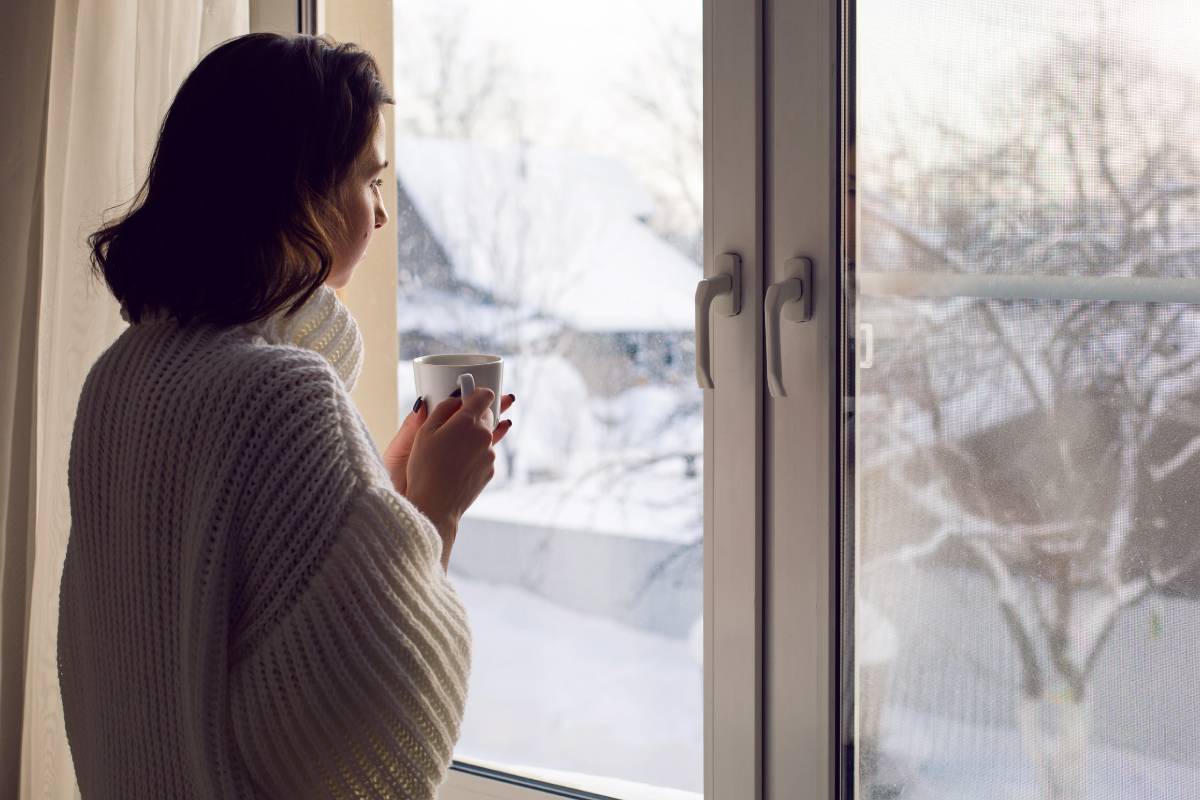 Woman holding a mug, peering out her window with drapes for winter hanging at the side at Phillips Paint & Decorating Center near Lancaster, PA