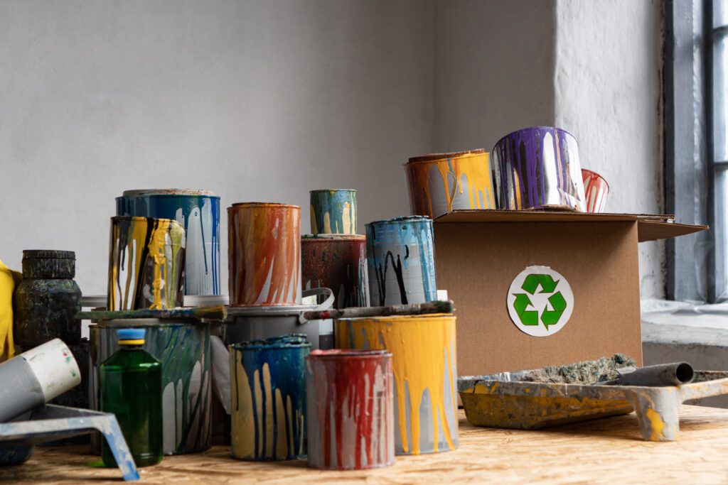 A collection of several old, empty paint cans with a box featuring a recycle logo