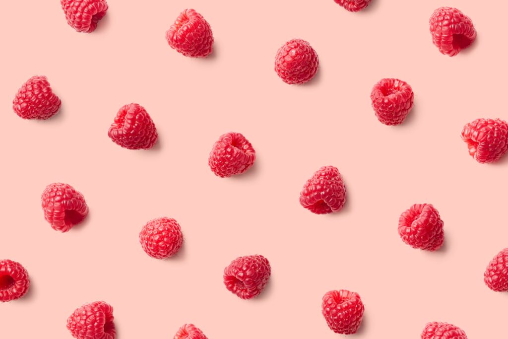 An image of several fresh raspberries in a repeating pattern on a light pink background